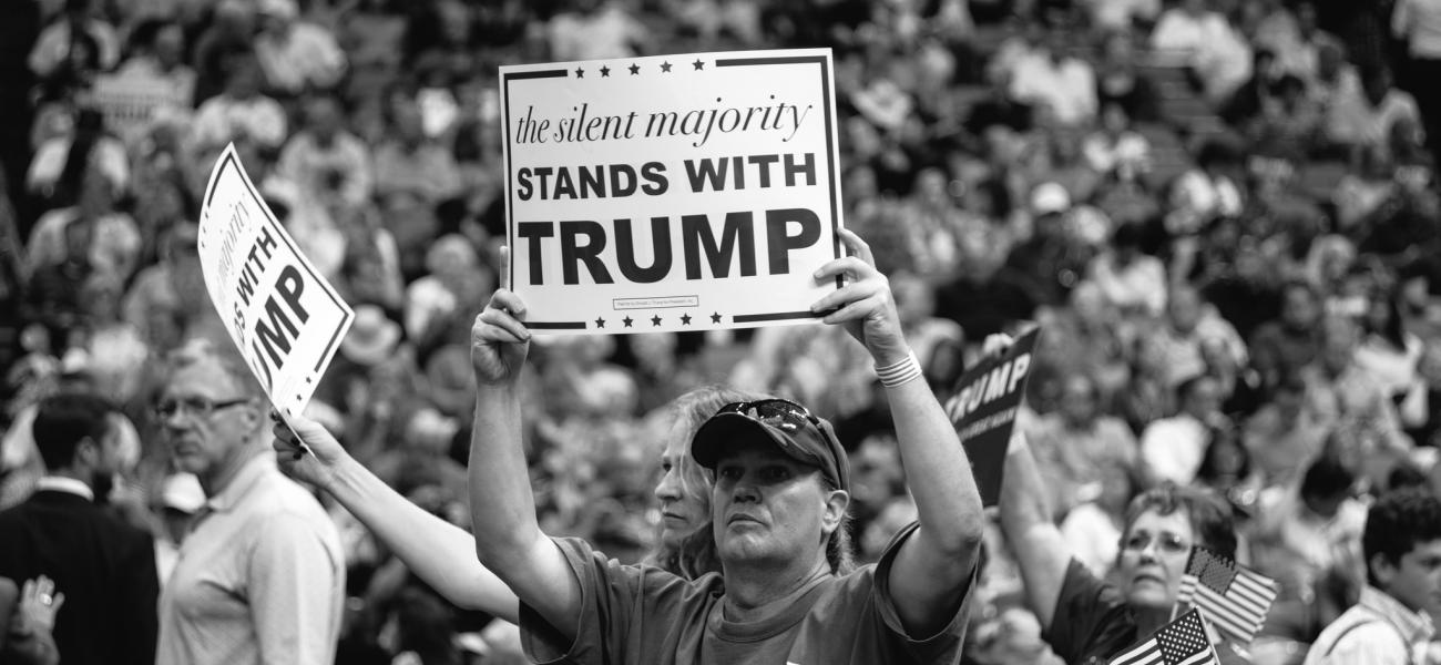 Man in the middle of a rally holding up a sign that reads "the silent majority stands with Trump."