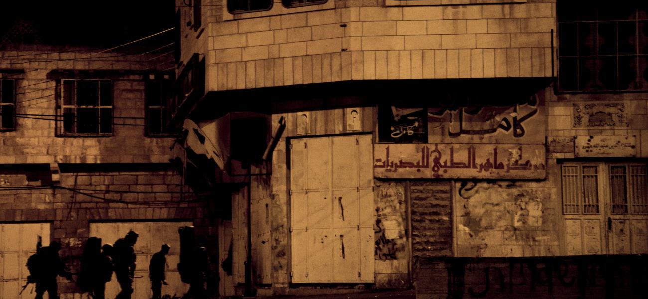 Soldiers file into a building bearing Arabic script.